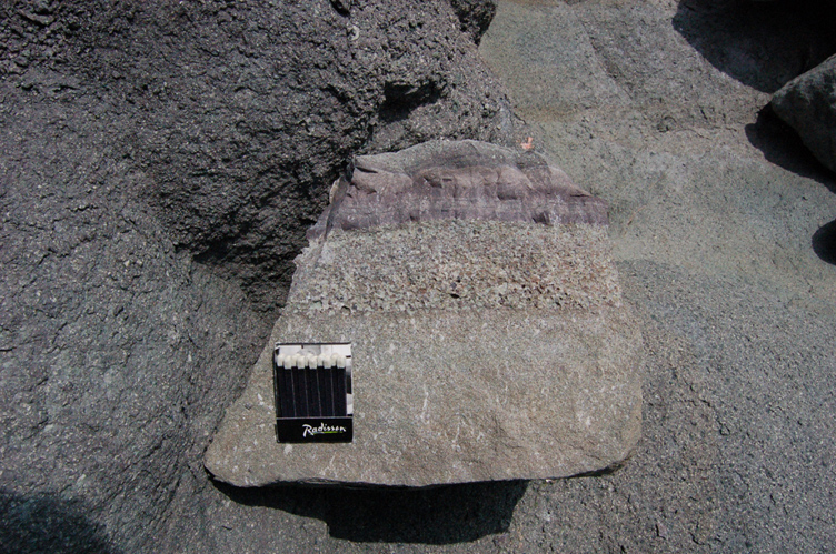 Fine epiclastic sediments (purple color) over coarse epiclastics and the latter over fine-grained andesite (loose piece of rock on the beach).