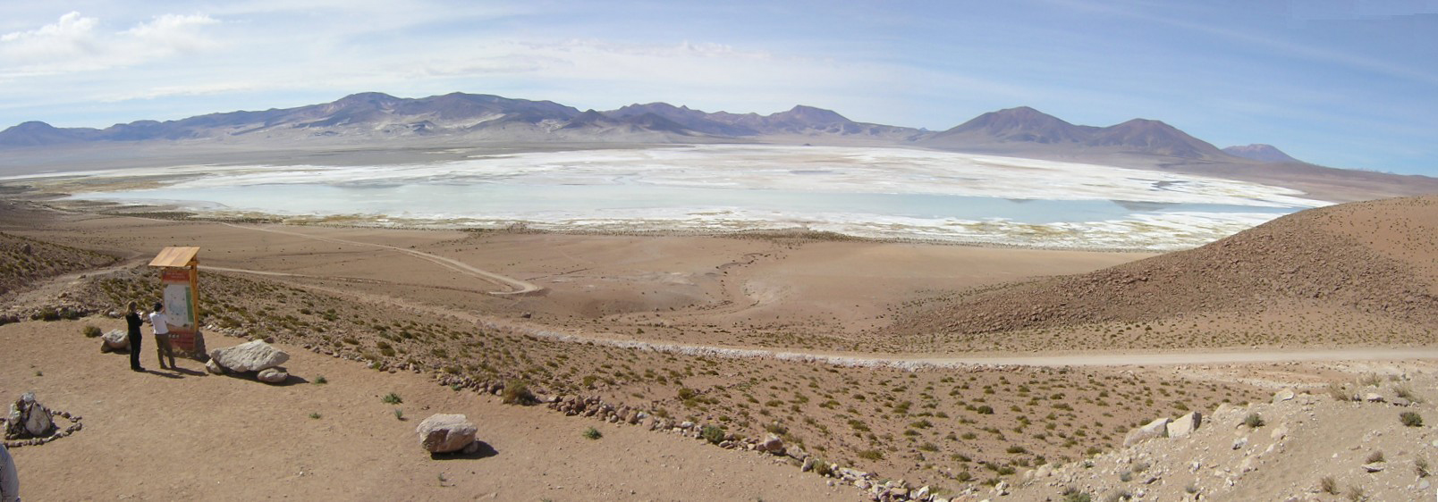 Panoramic view of the Salar de Huasco. In the center of the salt flats the ephemeral shallow waters, in the background the eroded volcanoes of the Mio-Pliocene, and in the foreground the viewpoint of the salt flats seated on the Huasco Ignimbrite (Miocene). The salts cover a surface area of about 50 km<sup>2</sup>.